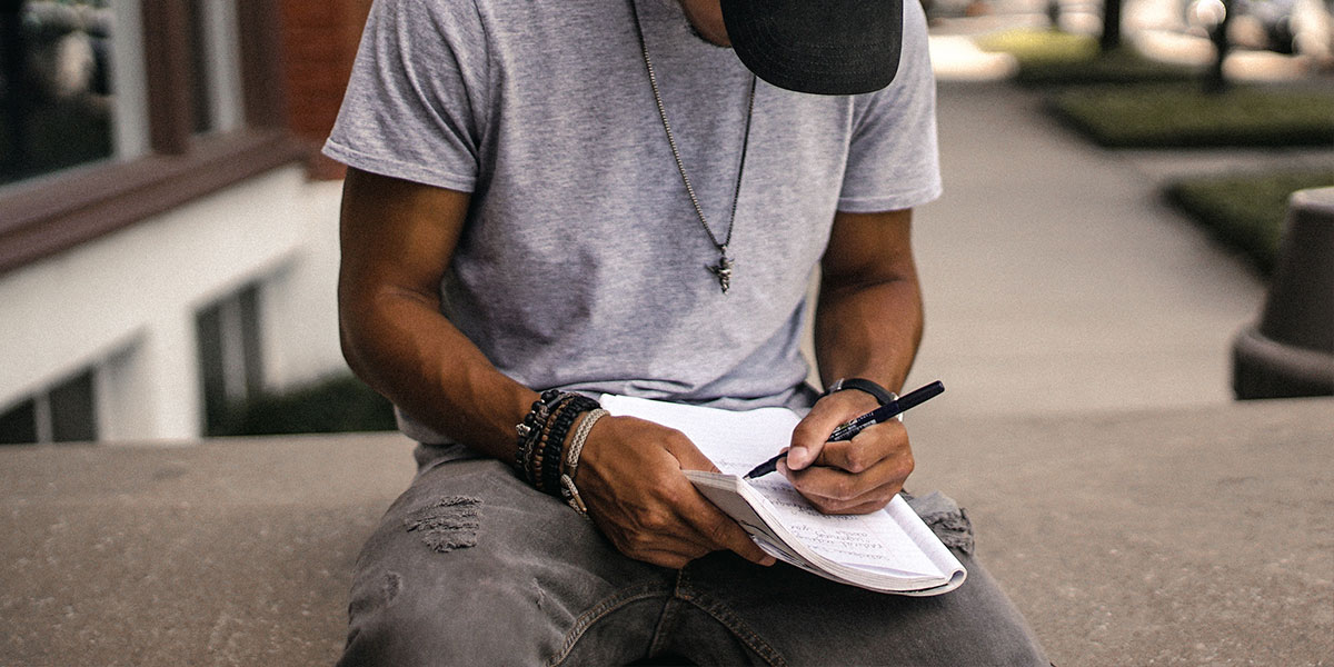 person in black adidas cap sitting on bench writing on notebook